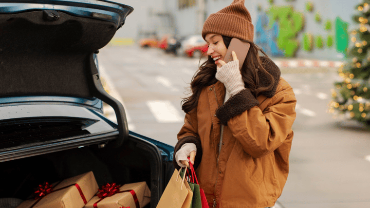 Woman packing holiday gifts into her vehicle while talking on her cell phone