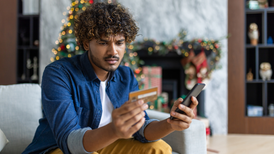 Young man confused while looking at his phone and holding his credit card. He is being cautious with his phone and email, searching for scams. 