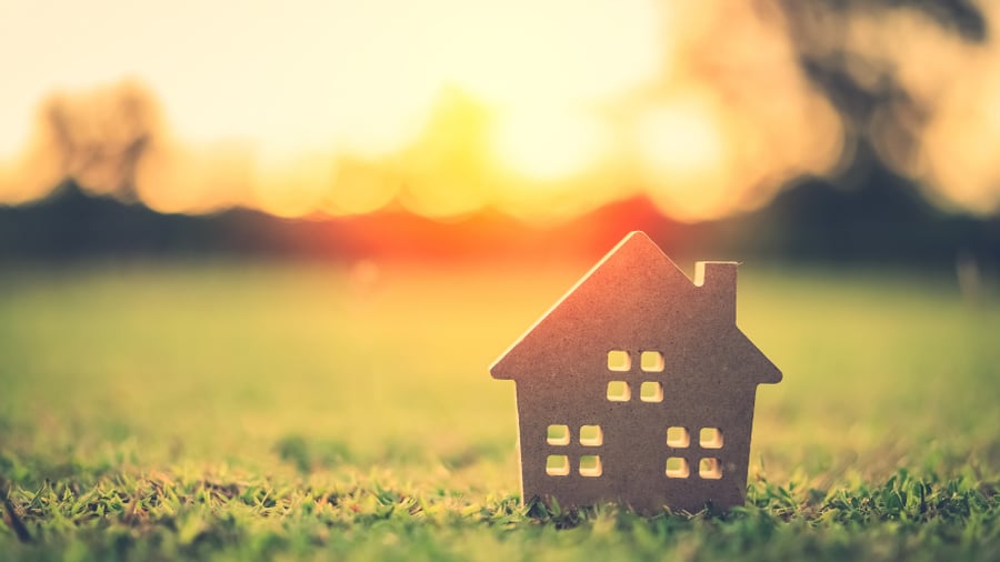 A home sitting on lush green grass with the sun shining, symbolizing spring homeownership.