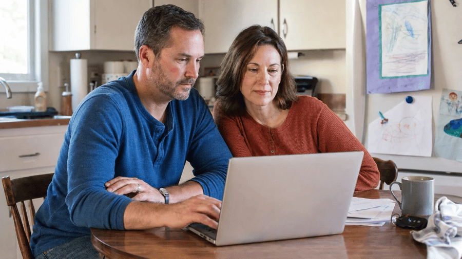 Couple sitting at kitchen table researching information on vehicle financing on their laptop computer 