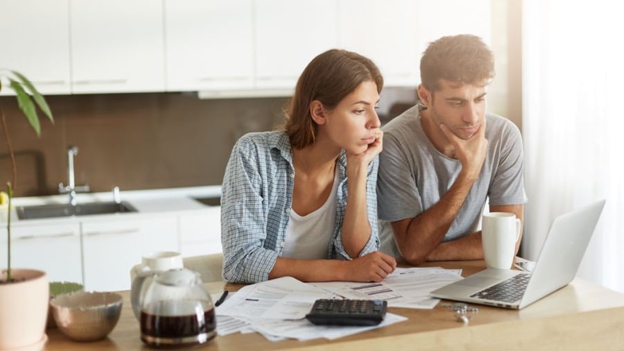 Young man and woman, sitting at their kitchen table, looking at their laptop. They have papers, a calculator, and some coffee as well. They are reviewing their IRA and taxes. 