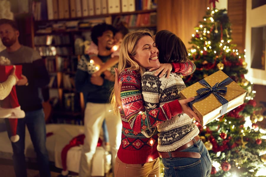 Friends hugging each other after exchanging gifts in front of a Christmas tree