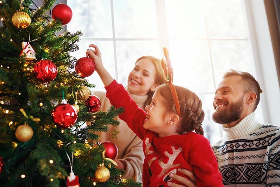 Parents and their daughter putting ornaments on a christmas tree