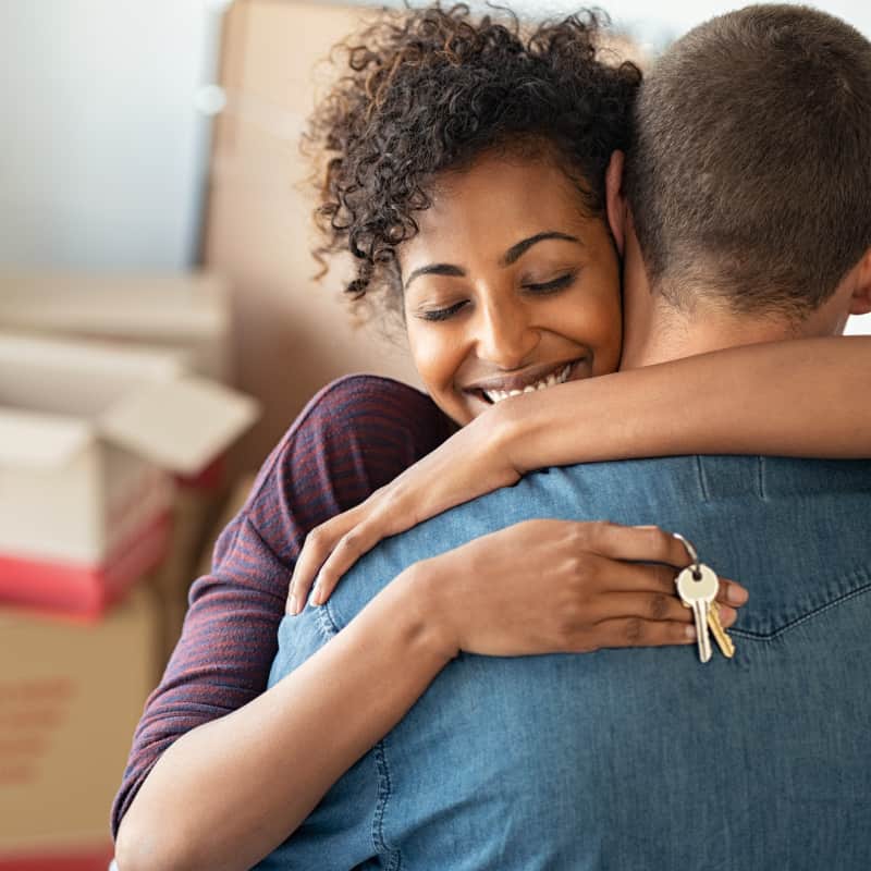 Woman and man giving each other a hug, in their new dream home! The woman is happy and holding the keys to the new home.