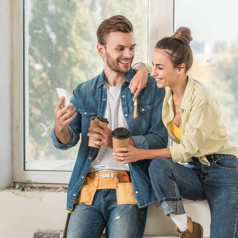 Man and woman completing a home improvement project in their home. They are happy and working with a ladder and painting.