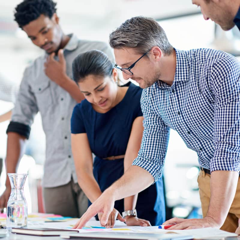 A team of coworkers in the office, working together to make a business plan. The team is diverse and excited to collaborate.
