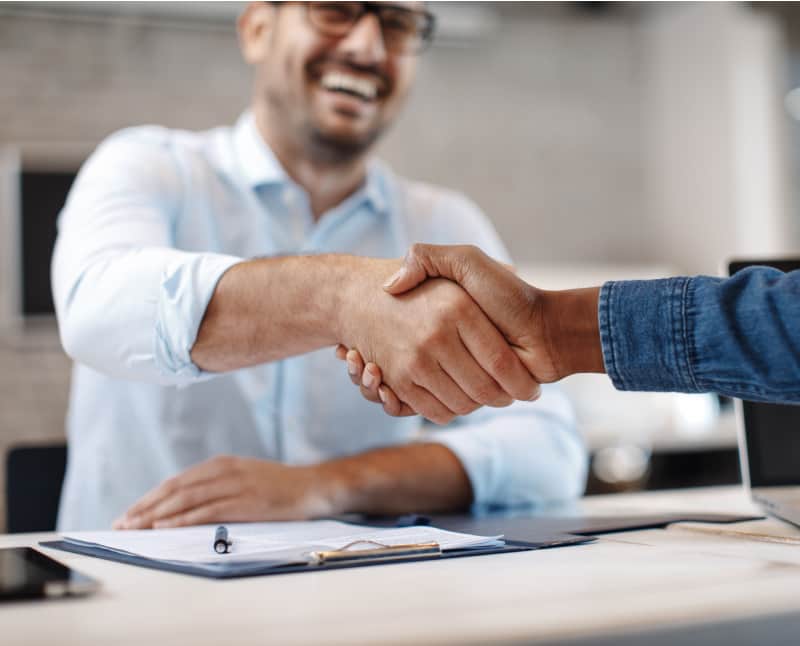 Two people in the branch office, shaking hands on the closing of a business project. The member is happy to have a business partnership.