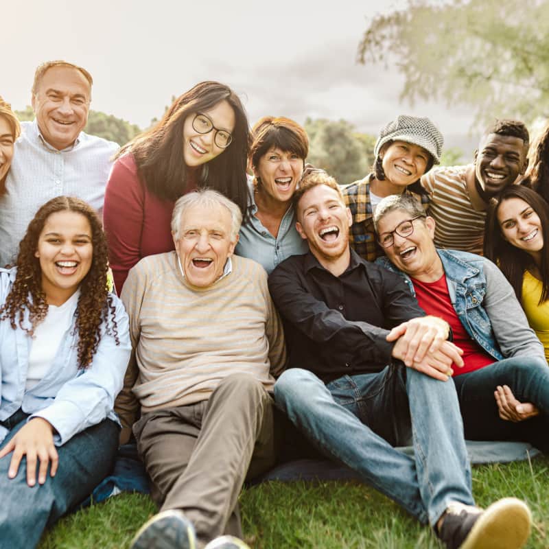 Happy multigenerational group of people having fun sitting on the grass at a community public park.