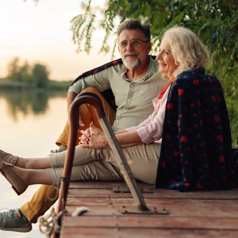 Happy senior couple relaxing by the lake, enjoying retirement together, with financial safety and reliability.