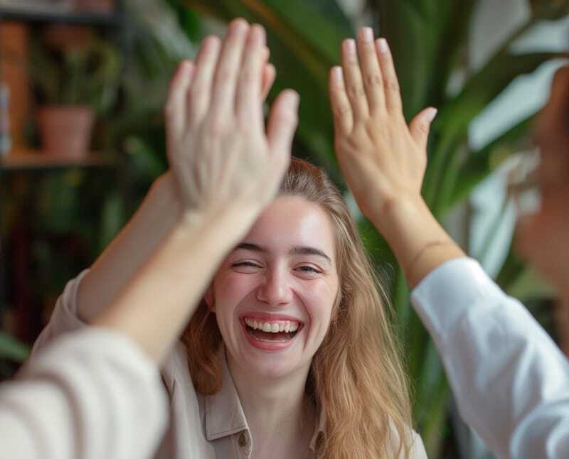Financial advisors surround a woman as they congratulate her and give her a high-five in the office. They are providing authentic care, and she is achieving financial peace of mind.