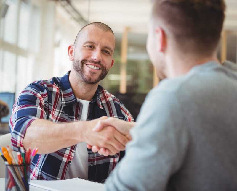 A financial advisor is meeting with a young man, shaking hands in an office. The young man is receiving a personalized experience that is a mutual benefit to both people.